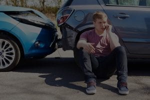 man sits next to his car on his phone after a crash