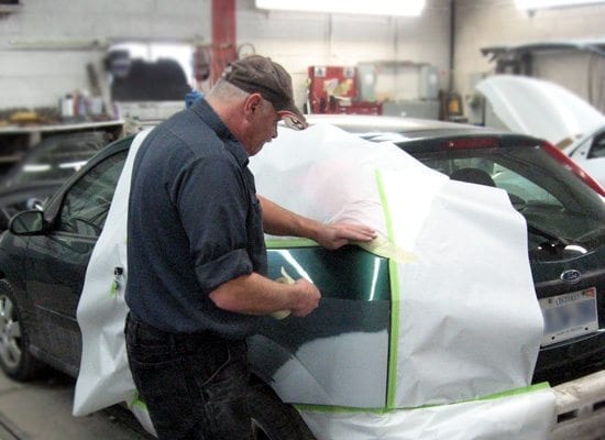 A mechanic works on repainting a car inside a car repair shop